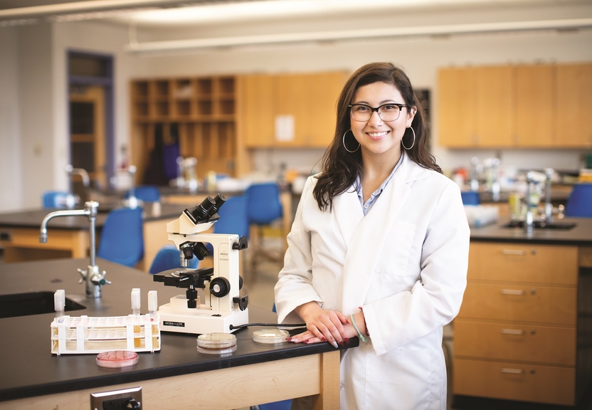 Student smiling next to a microscope