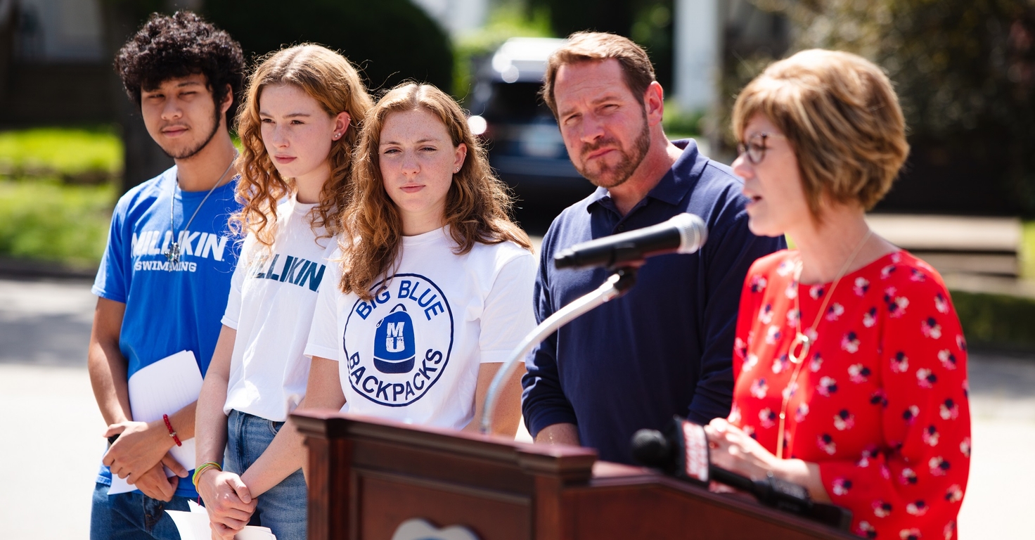 Four people listening to a speaker at a podium