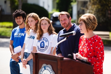 Four people listening to a speaker at a podium