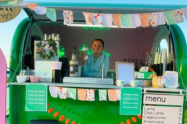 Image of green coffee trailer with young woman posing with beverage