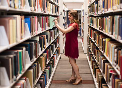 student pulling book from bookshelf