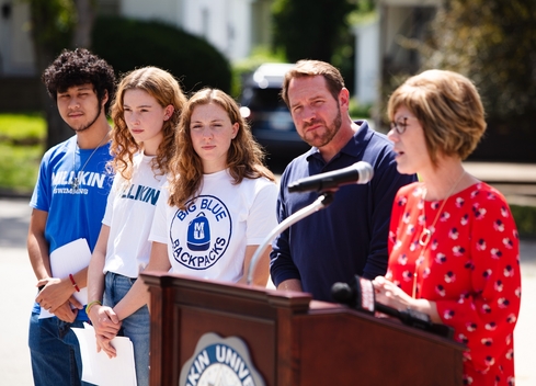 Four people listening to a speaker at a podium