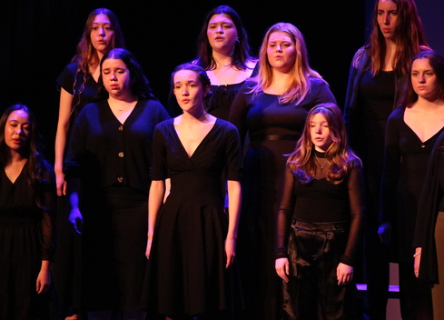 Treble Choir singing in front of black backdrop.