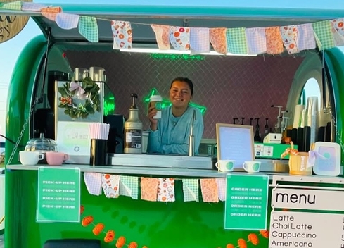 Image of green coffee trailer with young woman posing with beverage